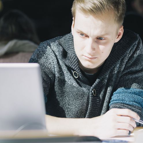 Junger Mann schaut auf den Bildschirm eines Laptops.