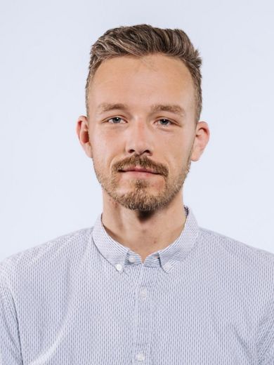 Auf dem Foto ist Florian Buhlrich zusehen. Er hat blonde, hochgelegte Haare und einen Bart. Er trägt ein hellblaues Hemd. 