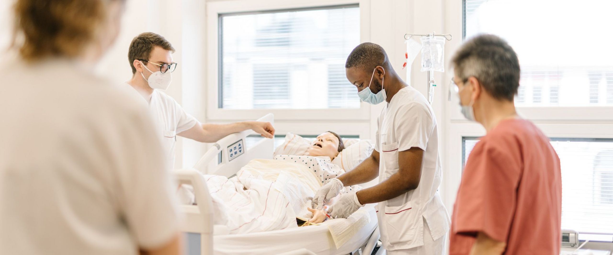 Pflegestudierende üben an einem Krankenhausbett mit einer Puppe im Simulationszentrum des Studiengangs.