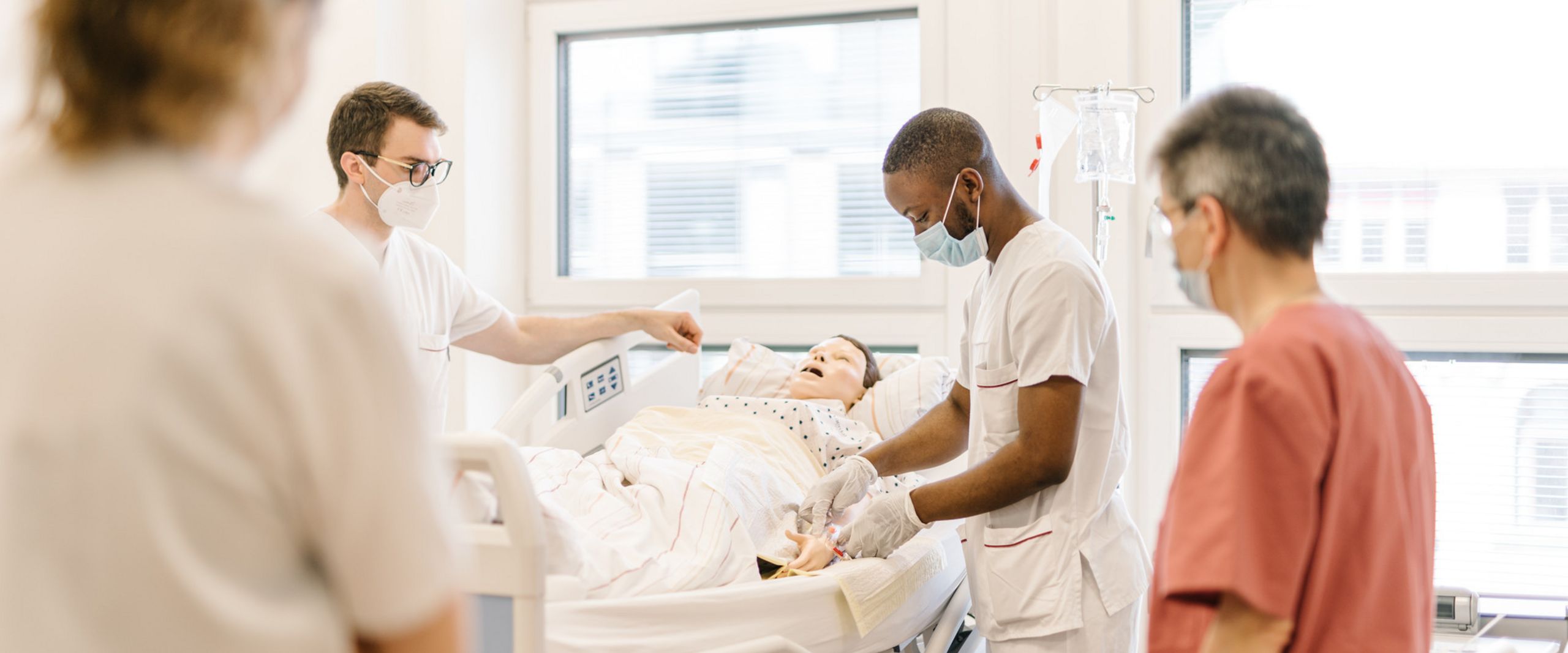Pflegestudierende &uuml;ben an einem Krankenhausbett mit einer Puppe im Simulationszentrum des Studiengangs.