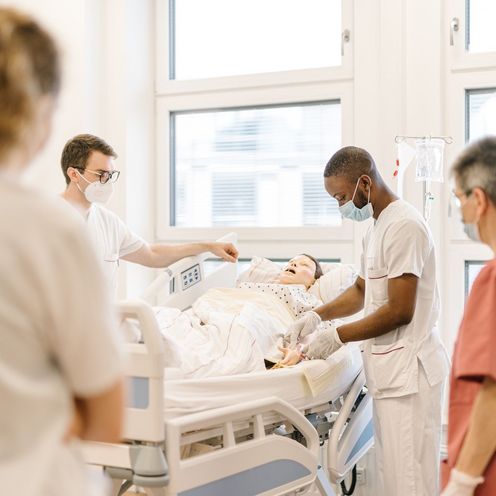 Pflegestudierende &uuml;ben an einem Krankenhausbett mit einer Puppe im Simulationszentrum des Studiengangs.