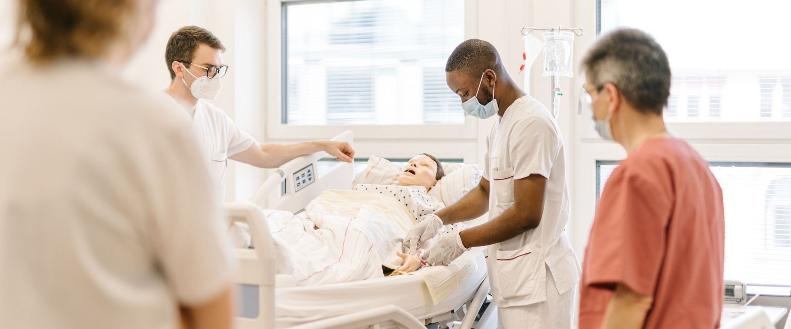 Pflegestudierende üben an einem Krankenhausbett mit einer Puppe im Simulationszentrum des Studiengangs.