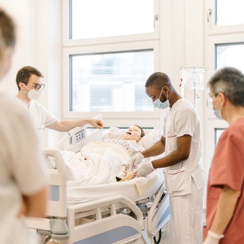 Pflegestudierende &uuml;ben an einem Krankenhausbett mit einer Puppe im Simulationszentrum des Studiengangs.
