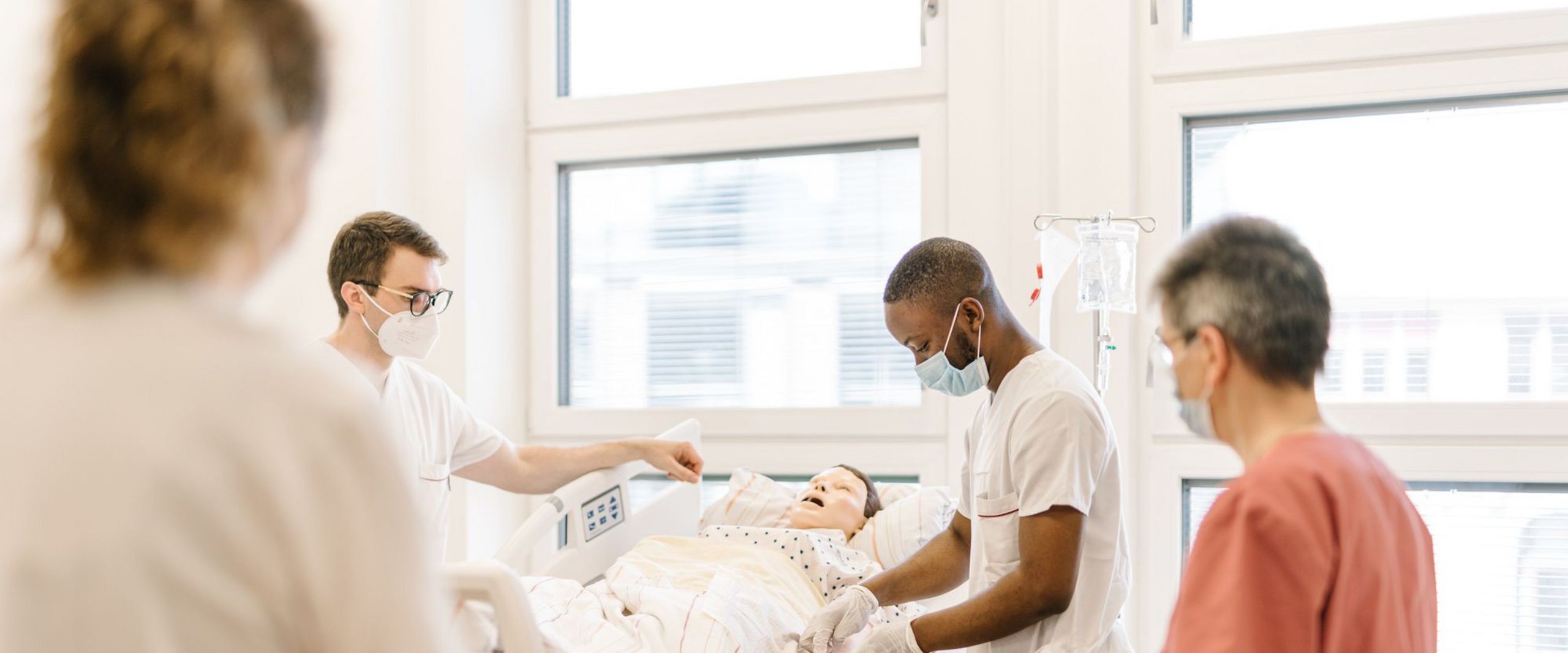 Pflegestudierende üben an einem Krankenhausbett mit einer Puppe im Simulationszentrum des Studiengangs.