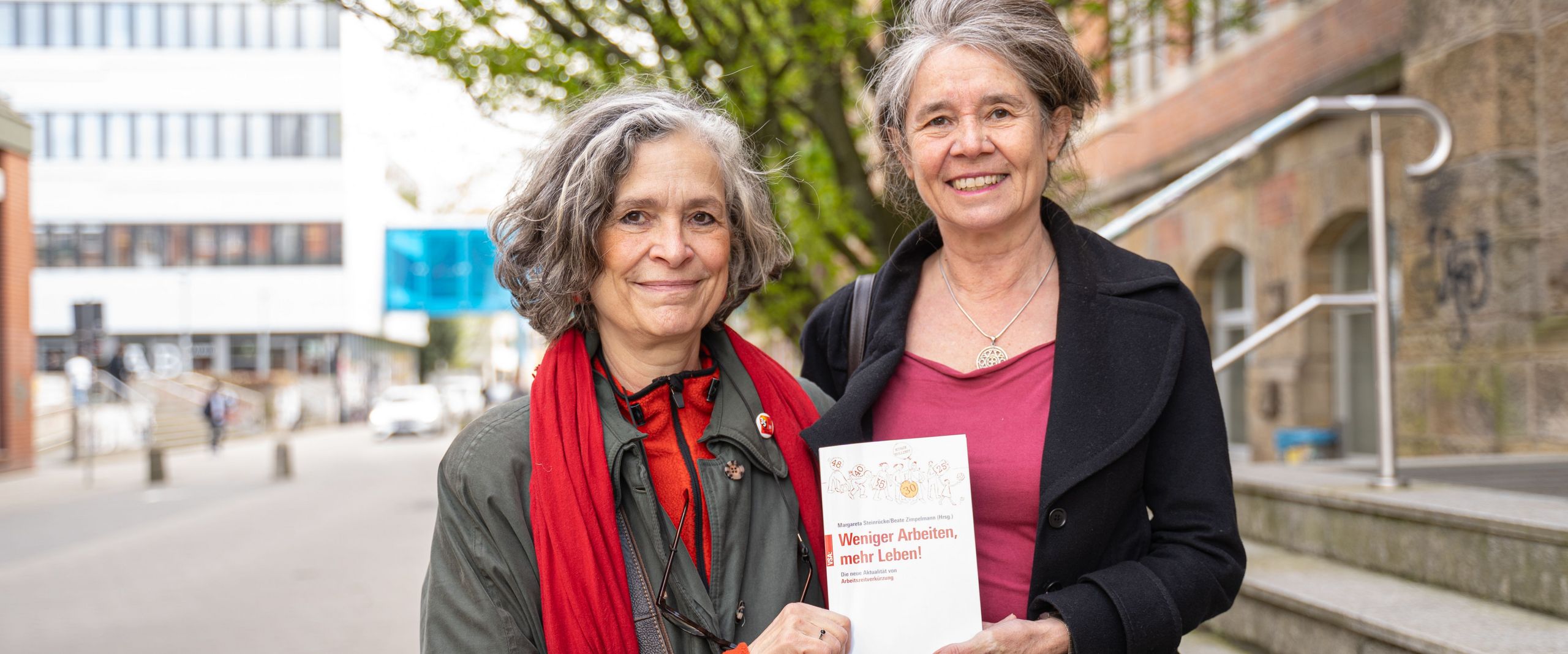 Zwei Frauen halten gemeinsam ein Buch und lächeln in die Kamera