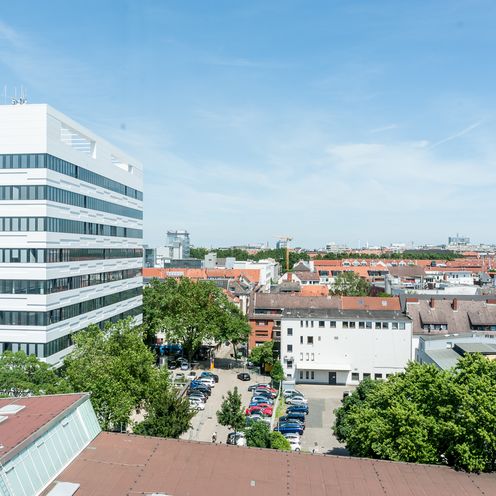 Foto von oben auf ein wei&szlig;es Hochhaus mit H&auml;usern und Gr&uuml;n drumherum