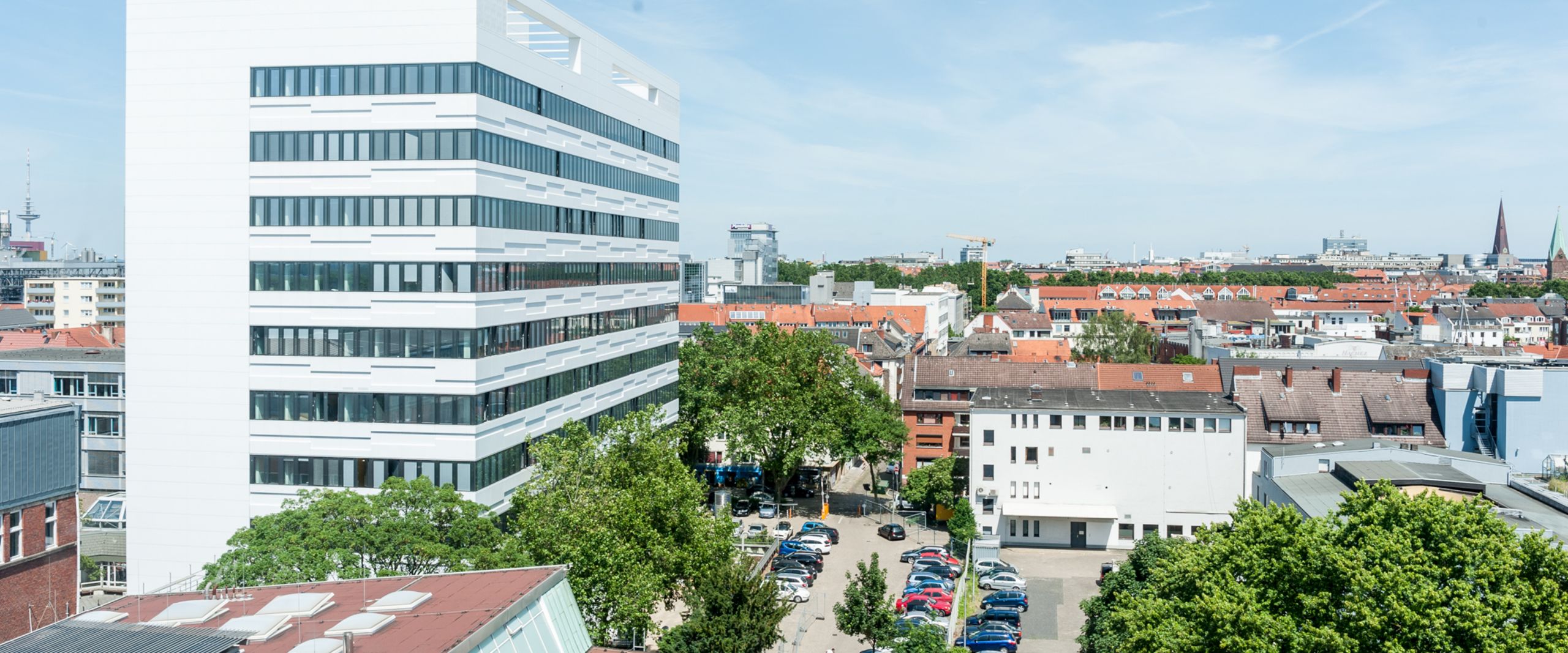 Foto von oben auf ein weißes Hochhaus mit Häusern und Grün drumherum