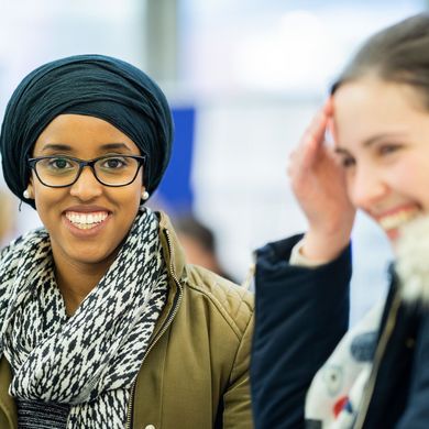 Zwei Studentinnen, beide lachen, die Studentin links ist im Fokus und sieht direkt in die Kamera
