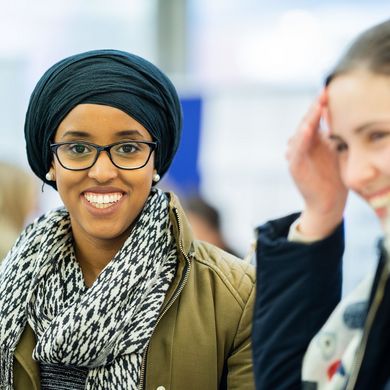 Zwei Studentinnen, beide lachen, die Studentin links ist im Fokus und sieht direkt in die Kamera