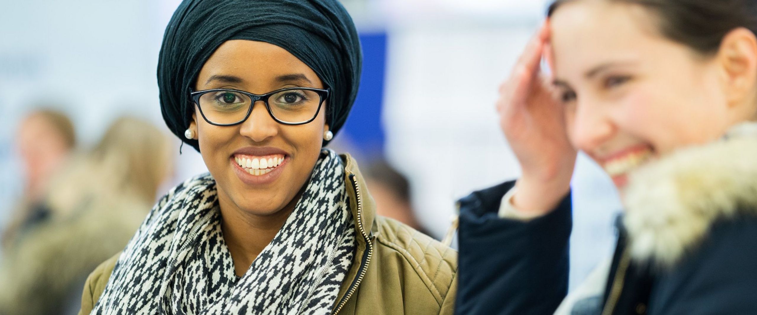 Zwei Studentinnen, beide lachen, die Studentin links ist im Fokus und sieht direkt in die Kamera