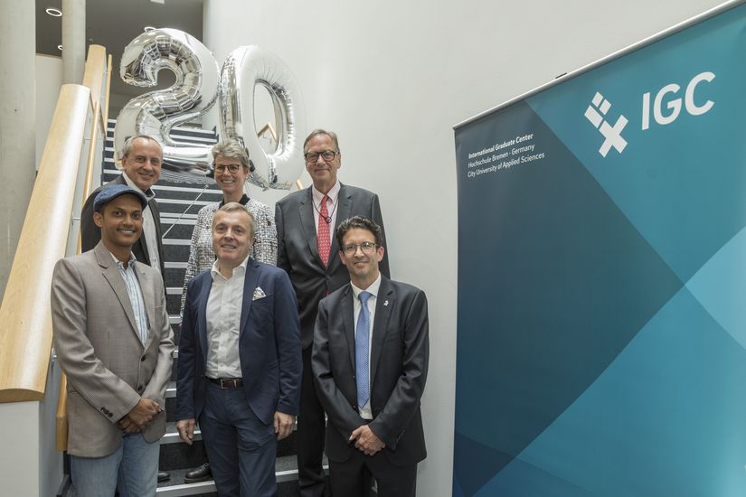 gruppenbild mit Männern und Frauen auf einer Treppe. Hinter ihnen schwebt eine 20 als zwei silberne Luftballons.