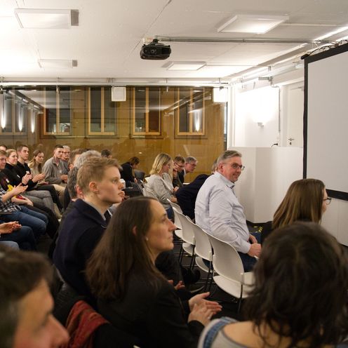 Das Bild zeigt einen Raum mit Zuh&ouml;rer:innen, die auf St&uuml;hlen sitzen.