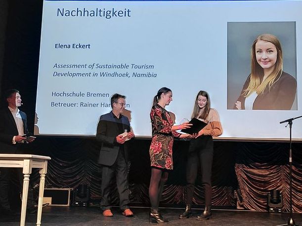 Studentin Elena Eckert steht auf einer B&uuml;hne und erh&auml;lt einen Preis von drei Jurymitgliedern der Deutschen Gesellschaft f&uuml;r Tourismuswissenschaft.