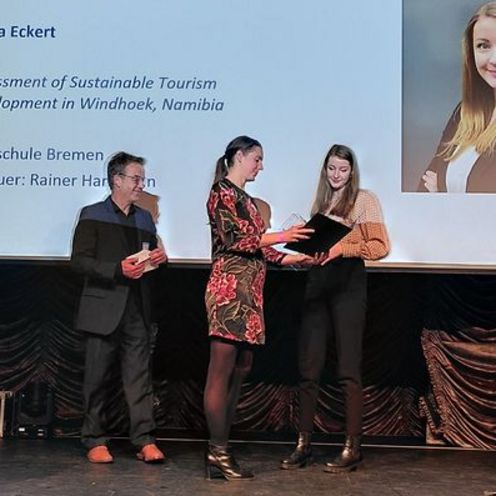 Studentin Elena Eckert steht auf einer B&uuml;hne und erh&auml;lt einen Preis von drei Jurymitgliedern der Deutschen Gesellschaft f&uuml;r Tourismuswissenschaft.