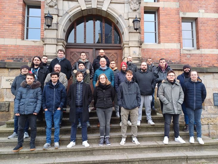 Eine Gruppe Studierender posiert auf einer Treppe vor dem M-Geb&auml;ude - einem Backsteingeb&auml;ude auf dem Campus der der Hochschule Bremen