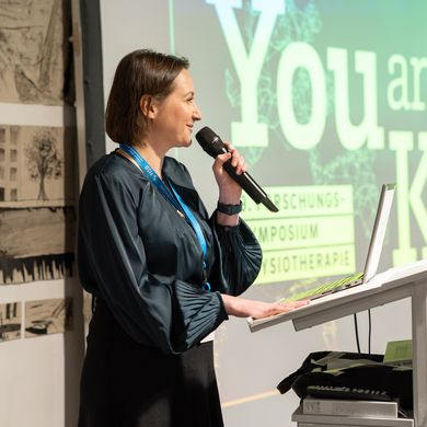 Auf dem Bild ist Prof. Dr. Annika Schwarz auf einer B&uuml;hne zu sehen. Neben ihr der Schriftzug "You are the Key" - das Motto des Symposiums