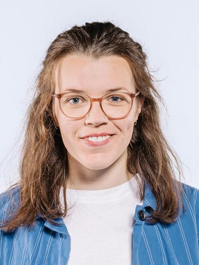 Auf dem Foto ist Luise Kilian zusehen. Sie hat braune, schulterlange Haare. Sie trägt eine Brille und ein weißes T-Shirt unter einem Himmelblauen Hemd. 