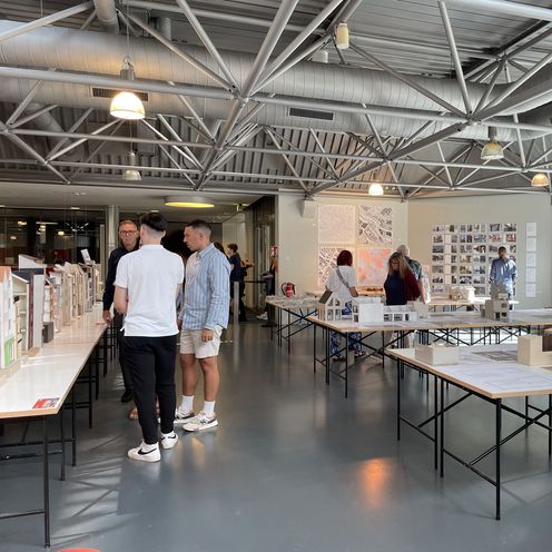 Architekturmodelle stehen auf Tischen in einem Raum. Menschen schauen sie sich an.