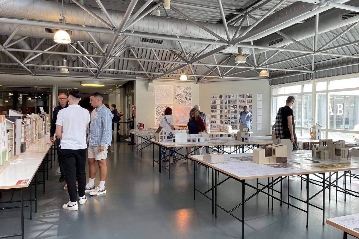 Architekturmodelle stehen auf Tischen in einem Raum. Menschen schauen sie sich an.