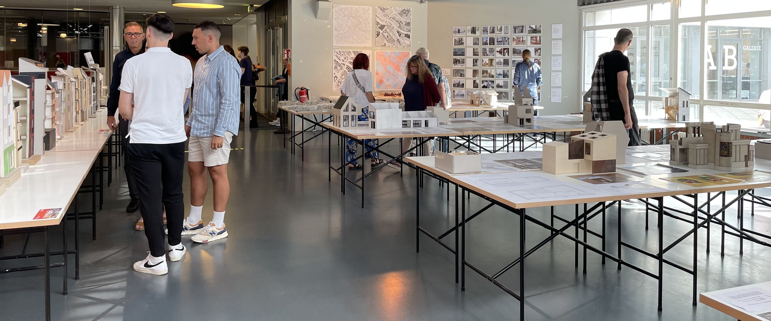 Architekturmodelle stehen auf Tischen in einem Raum. Menschen schauen sie sich an.