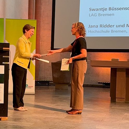 Zwei Frauen begr&uuml;&szlig;en sich an einem Podium