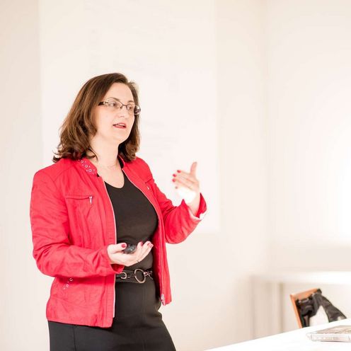 Auf dem Bild ist Jasminka Matevska zu sehen. Sie h&auml;lt einen Vortrag und tr&auml;gt einen roten Blazer. 