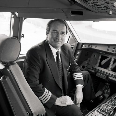 Mann sitzt in Uniform im Flugzeugcockpit und schaut in die Kamera