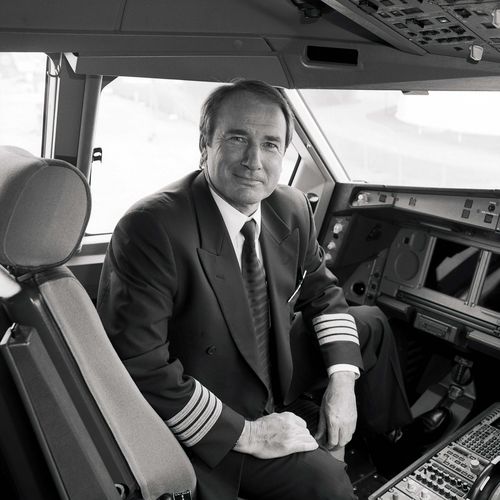 Mann sitzt in Uniform im Flugzeugcockpit und schaut in die Kamera