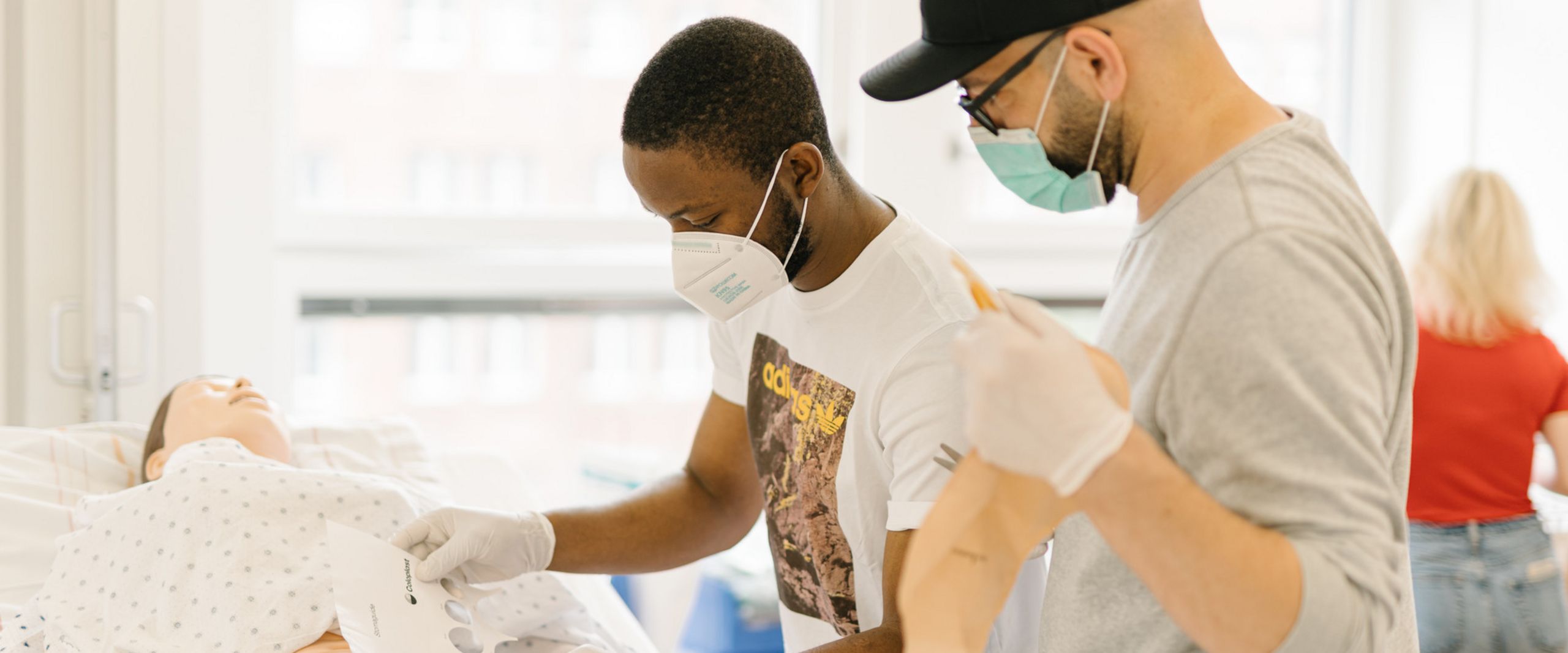 Pflegestudierende &uuml;ben an einem Krankenhausbett mit einer Puppe im Simulationszentrum des Studiengangs.