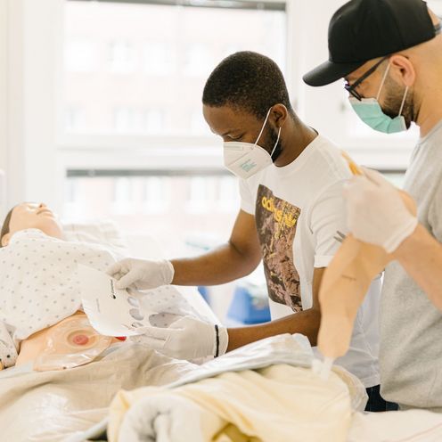 Pflegestudierende &uuml;ben an einem Krankenhausbett mit einer Puppe im Simulationszentrum des Studiengangs.