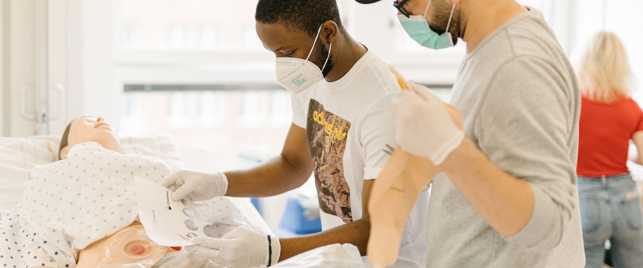 Pflegestudierende üben an einem Krankenhausbett mit einer Puppe im Simulationszentrum des Studiengangs.