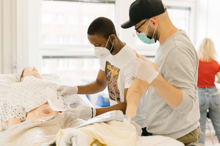 Pflegestudierende üben an einem Krankenhausbett mit einer Puppe im Simulationszentrum des Studiengangs.