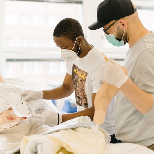 Pflegestudierende &uuml;ben an einem Krankenhausbett mit einer Puppe im Simulationszentrum des Studiengangs.