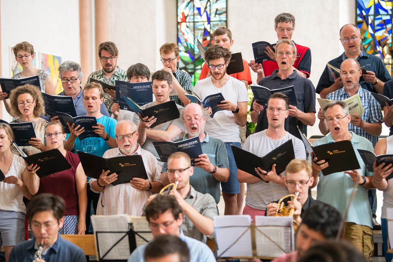 Frauen und Männer des Chors aufgereiht bei einem Auftritt mit Notenbüchern in den Händen.