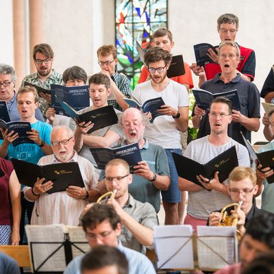 Frauen und Männer des Chors aufgereiht bei einem Auftritt mit Notenbüchern in den Händen.