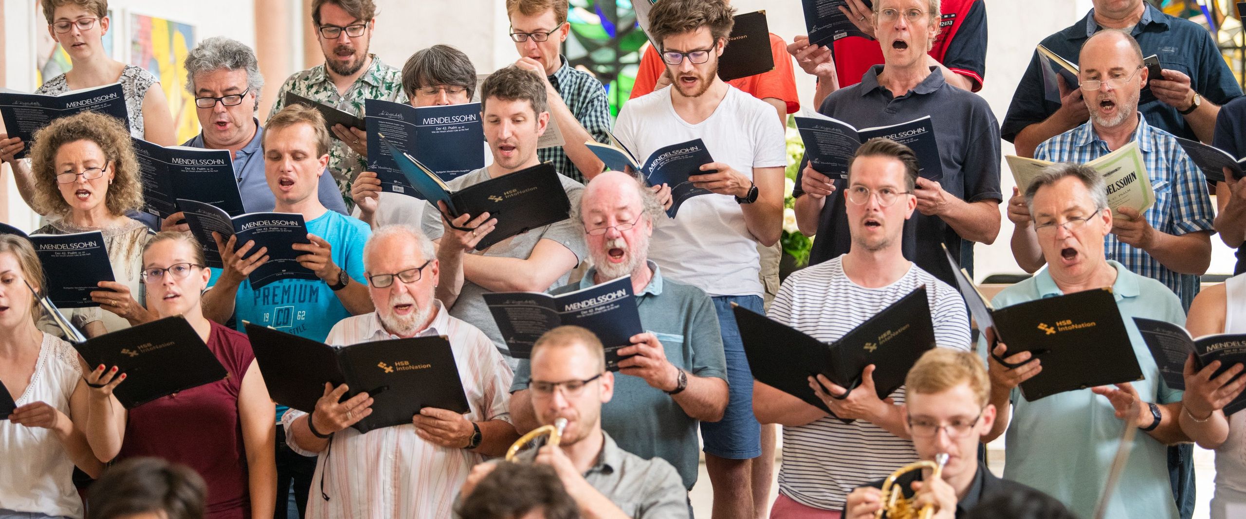 RS8548_20190629-0-218.jpg Frauen und Männer des Chors aufgereiht bei einem Auftritt mit Notenbüchern in den Händen.