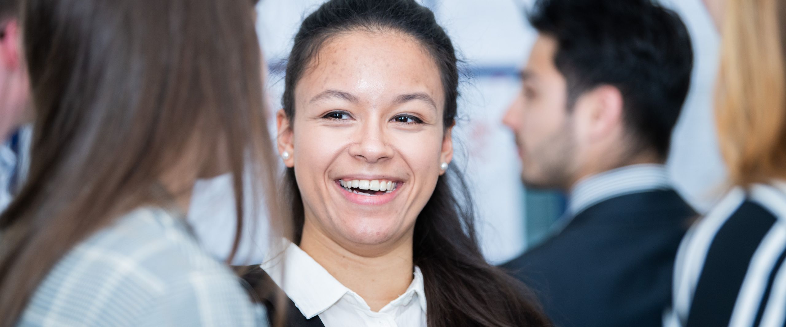 Frau steht zwischen Leuten und lacht in die Kamera