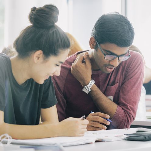 Eine Studentin und ein Student &uuml;ber Unterlagen gebeugt