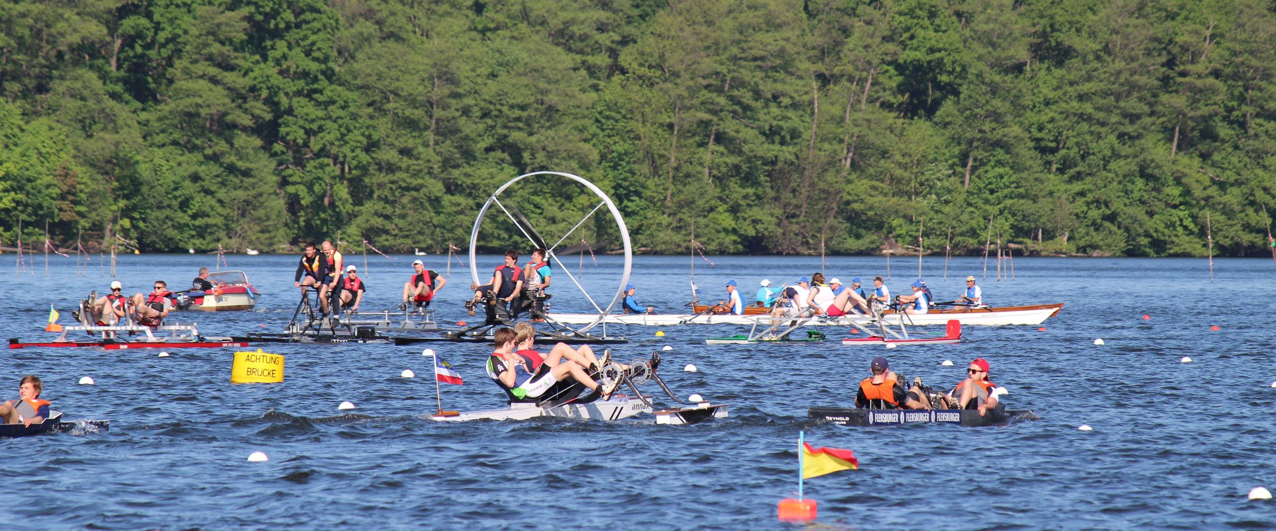 Studentische Tretbootteams bei einer Regatta auf einem See.