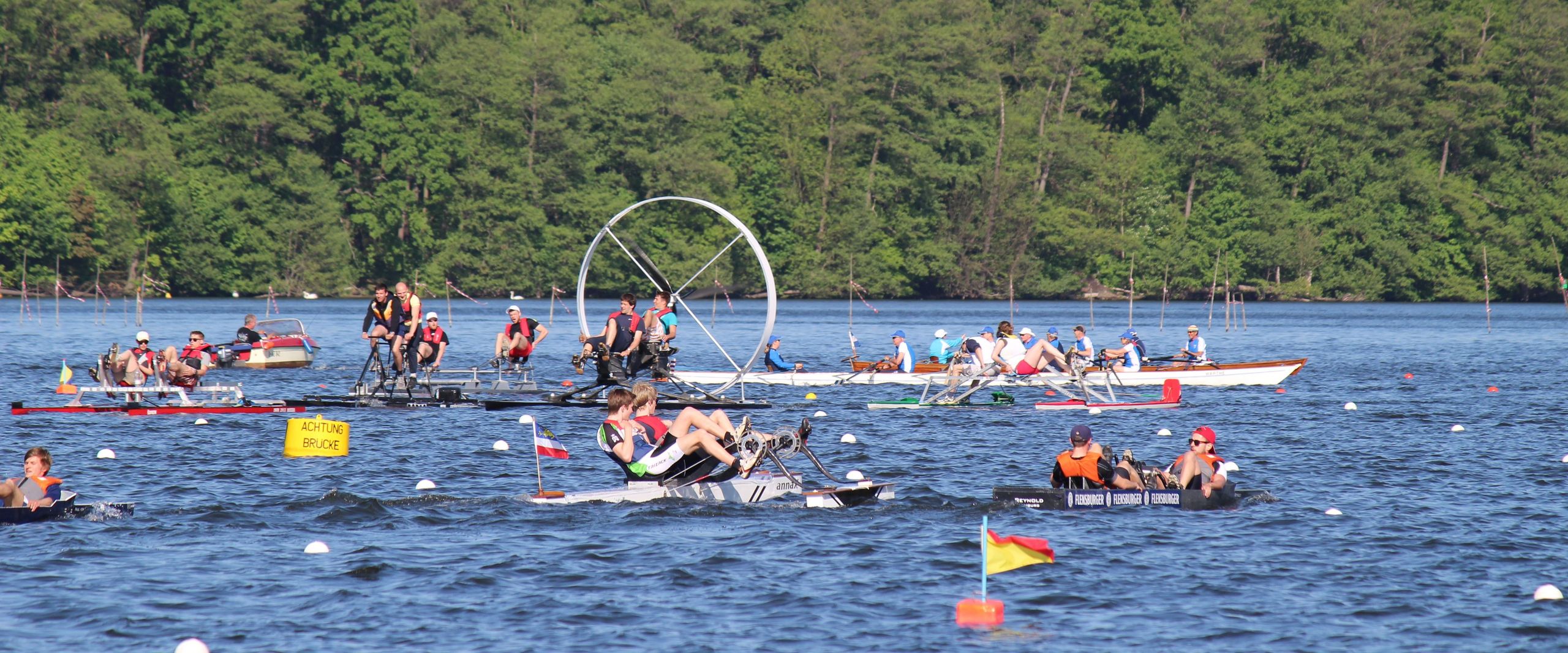 Studentische Tretbootteams bei einer Regatta auf einem See.