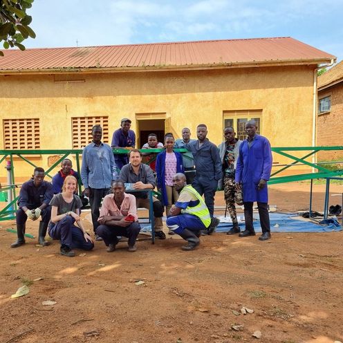 Gruppenbild mit M&auml;nnern und frauen vor einer H&uuml;tte.