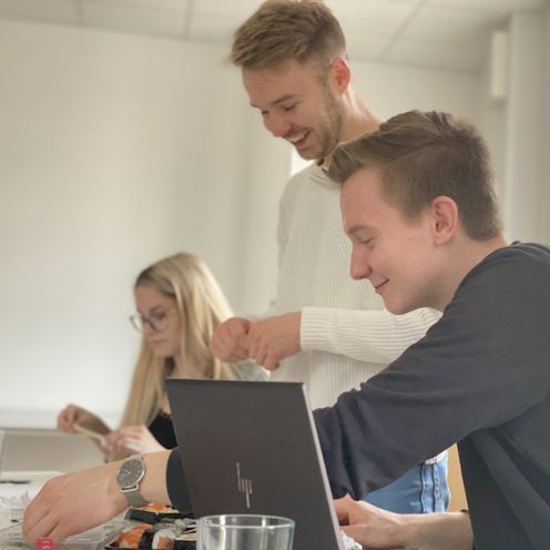 Zwei junge M&auml;nner und eine Frau arbeiten an Tischen.