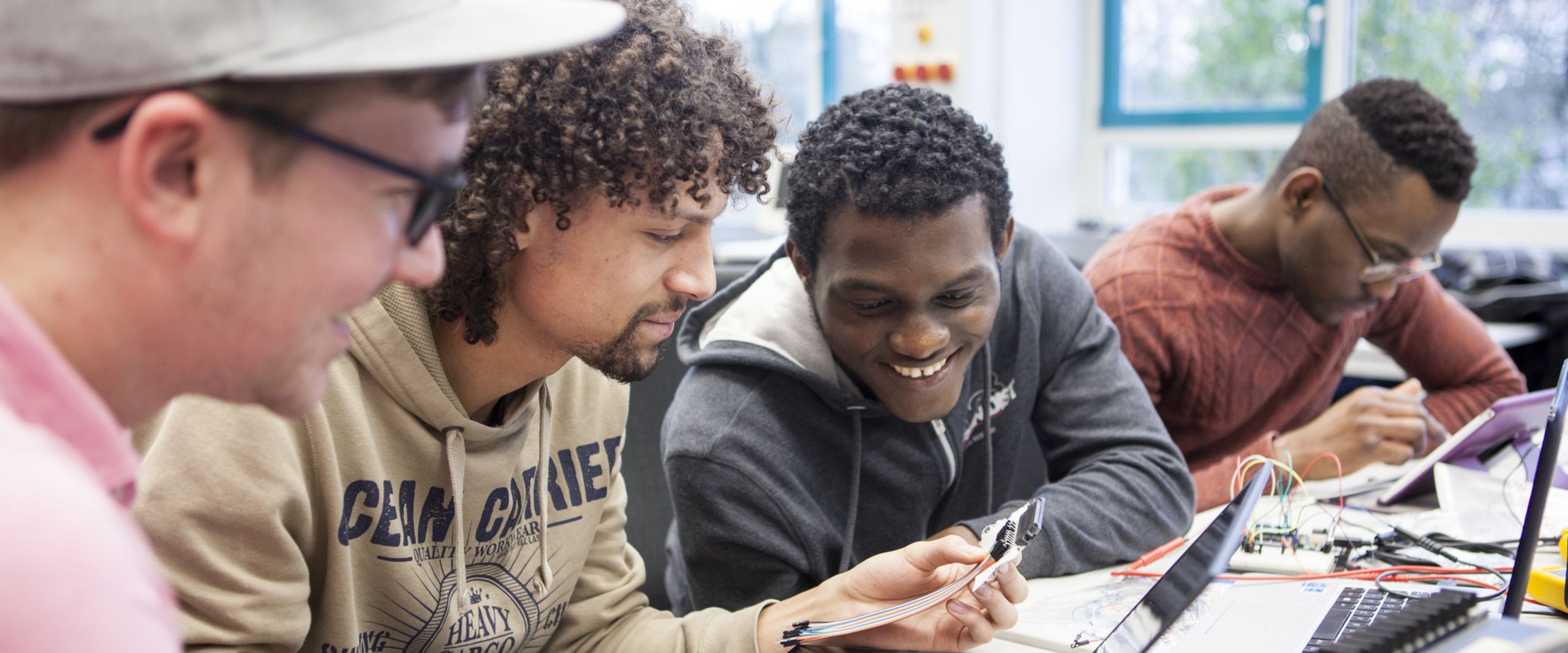 Studierende sehen schauen gemeinsam auf den Bildschirm eines Laptops.
