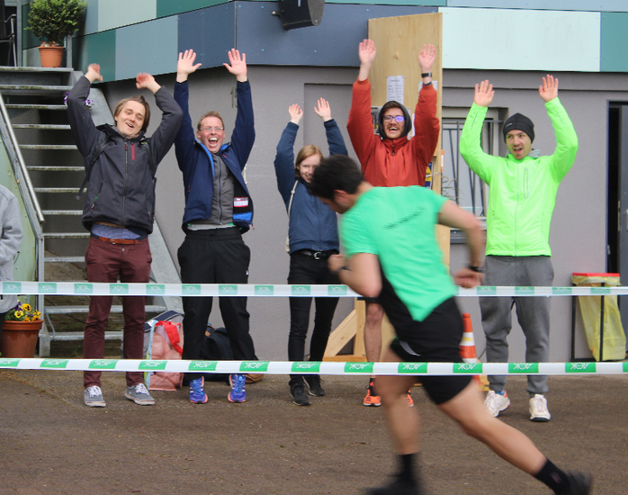 Ein sprintender L&auml;ufer und dahinter f&uuml;nf jubelnde Menschen.