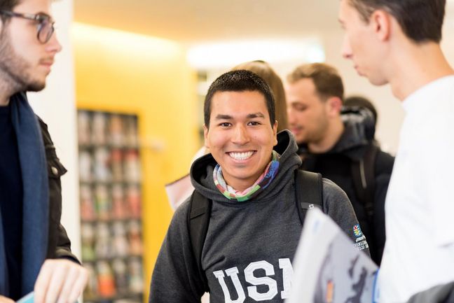 Welcome to campus Smiling student in a university hallway, surrounded by peers.