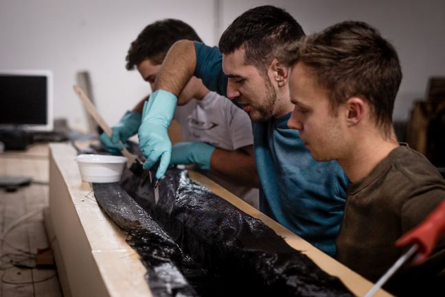 Drei Studierende arbeiten an einem Boot.