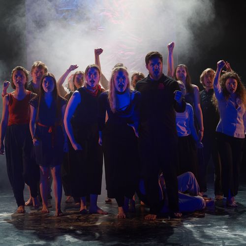 Dunkel gekleidete Menschen stehen auf einer B&uuml;hne. Es ist dunkel und Nebel umgibt sie.