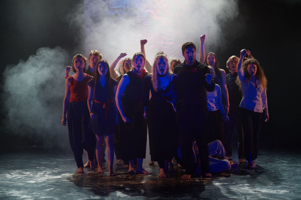 Dunkel gekleidete Menschen stehen auf einer B&uuml;hne. Es ist dunkel und Nebel umgibt sie.