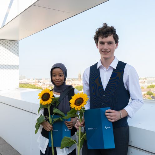 Preistr&auml;ger:innen der Sommerschau 2024 stehen nebeneiander auf einer Dachterrasse mit Blick auf Bremen. Sie halten Sonnenblumen und eine Urkunde in der Hand und l&auml;cheln.
