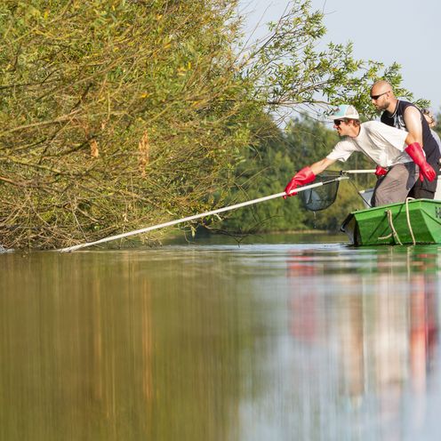 Menschen im Boot auf einem See am Rande eines Ufers. Sie fischen im Wasser.
